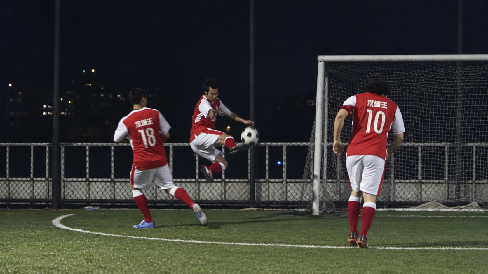 Three football players near the goal during a night-time game.