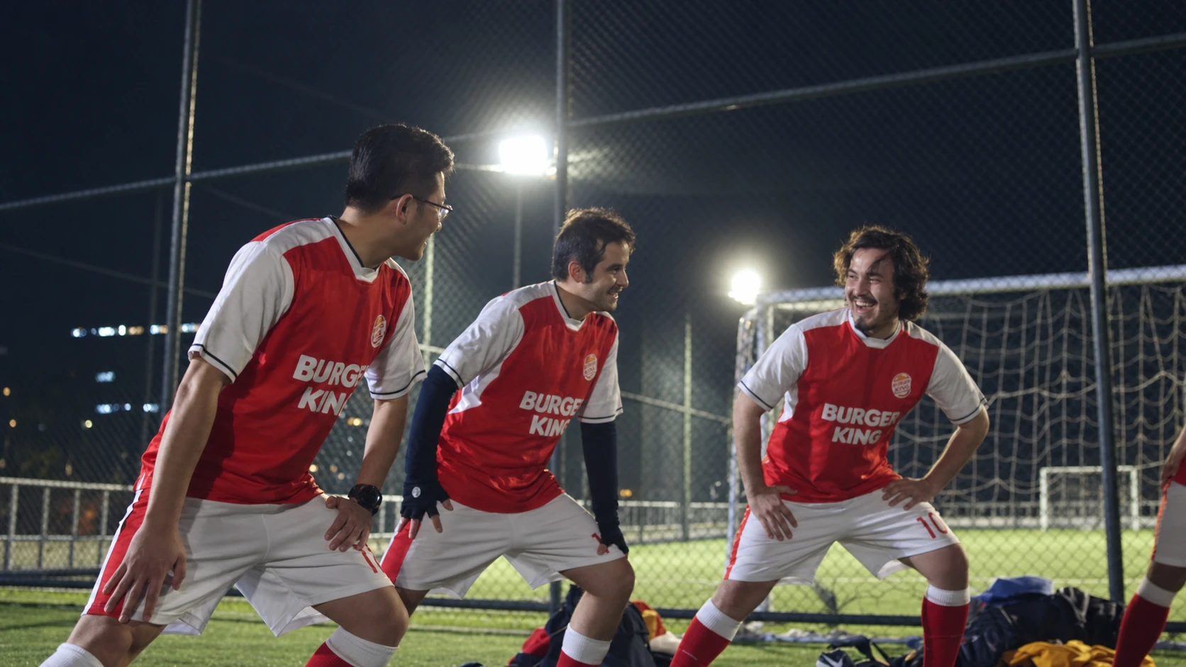 Team members in red and white football kits stretching together at night.