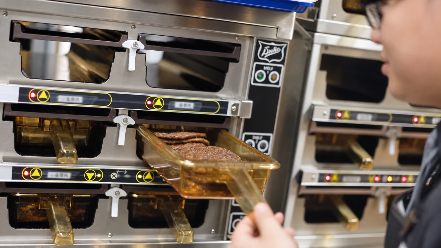 A kitchen team member lifting a tray beside the cooking equipment.