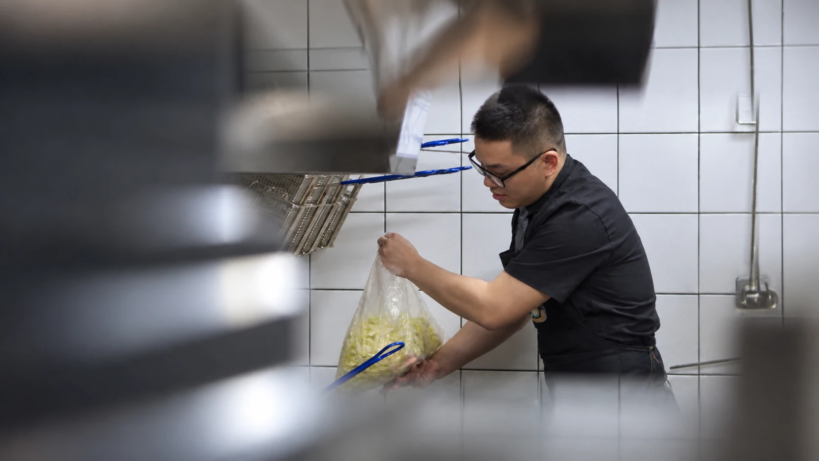 A kitchen team member handling a clear bag at a tiled workstation.