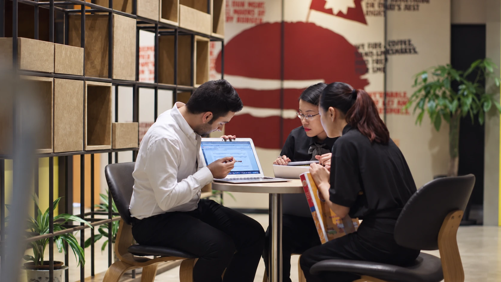 Three colleagues gathered around a laptop at a restaurant table.