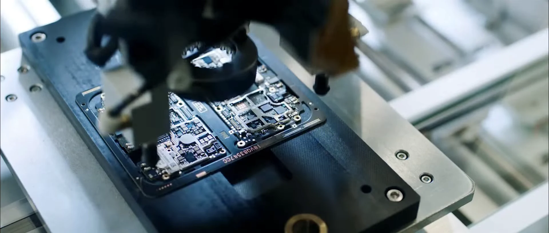 An automated fixture holds a smartphone circuit board beneath an inspection head.