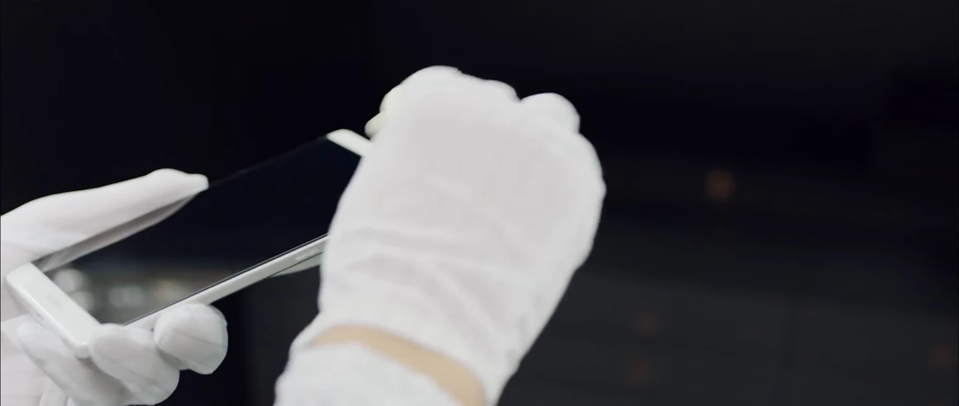 White-gloved hands inspecting and handling a smartphone.