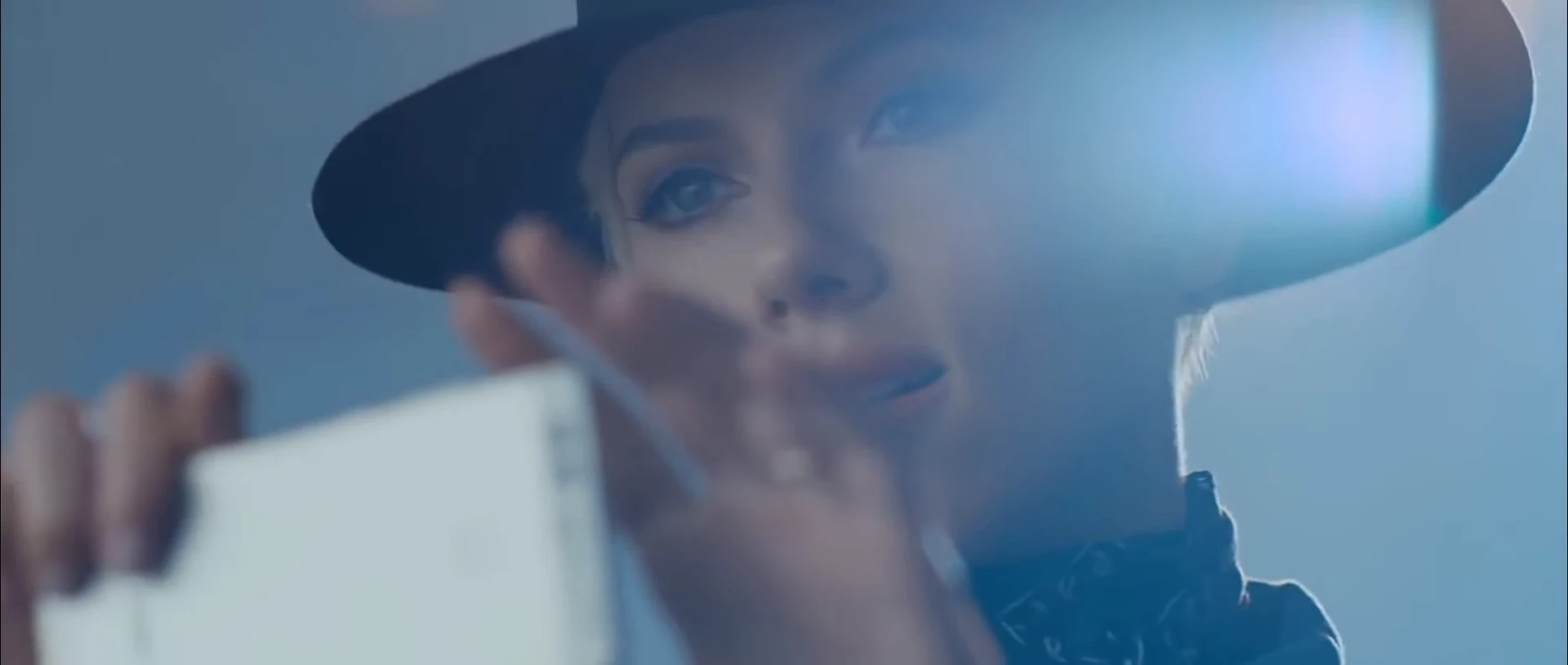 A woman in a dark hat holding up a smartphone toward the camera.