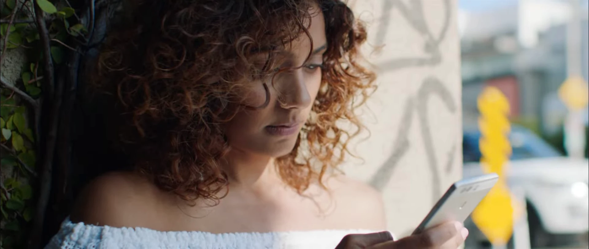 A woman with curly hair looking at a smartphone outdoors.