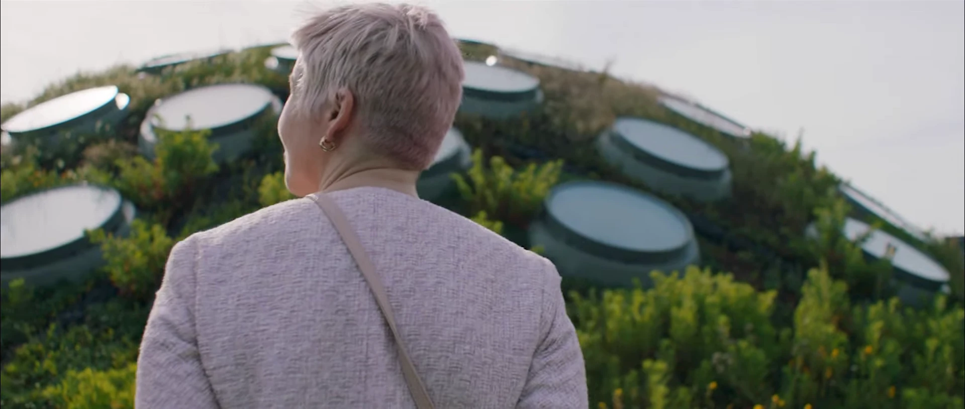 A woman seen from behind in front of a building covered in planting.