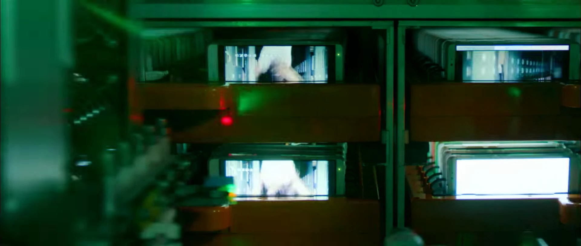 Several smartphone displays operating inside a green-lit testing machine.