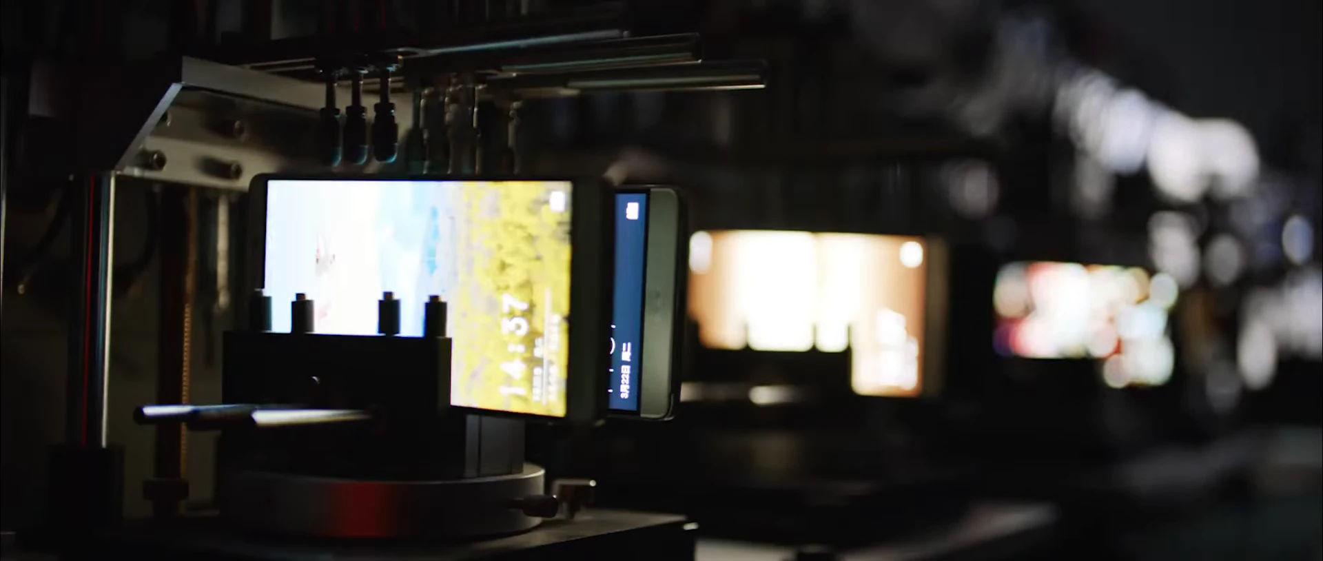 A row of smartphones displaying imagery in a testing rig.