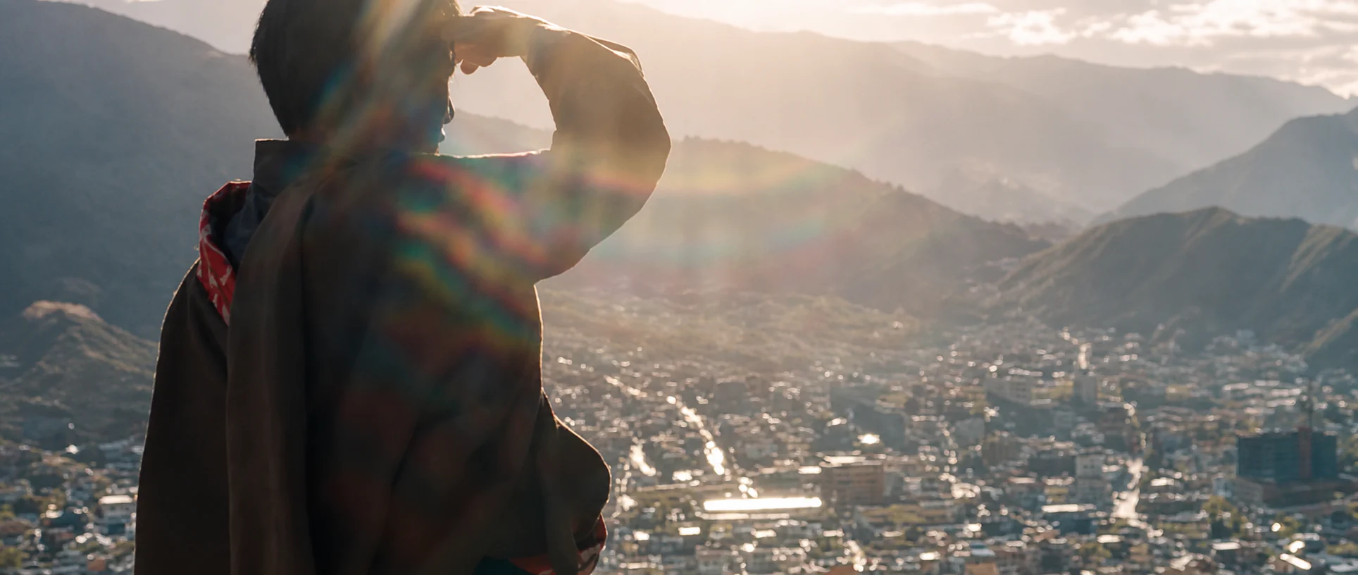 A person shielding their eyes while overlooking a mountain city.