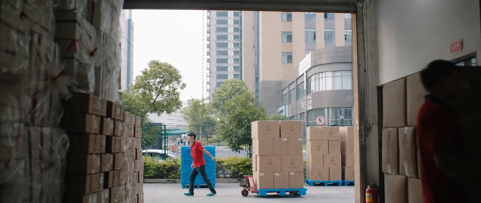 A worker pushing a cart stacked with parcels through a service lane.