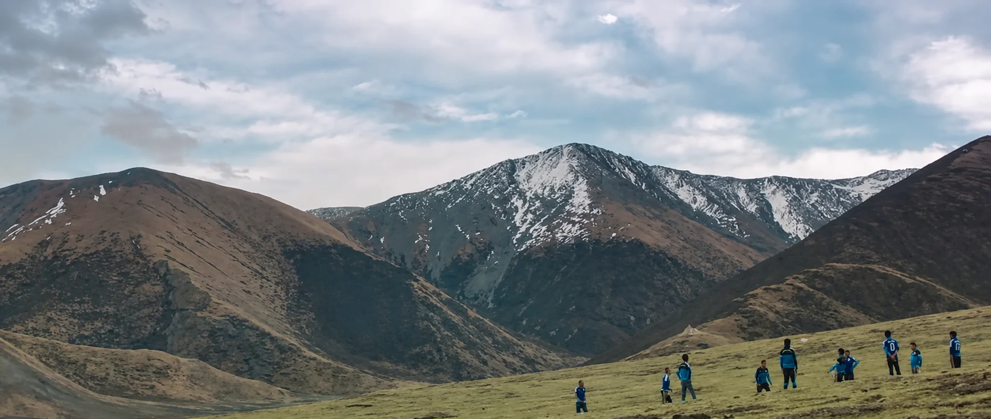 Hikers crossing open grassland below mountain ridges.
