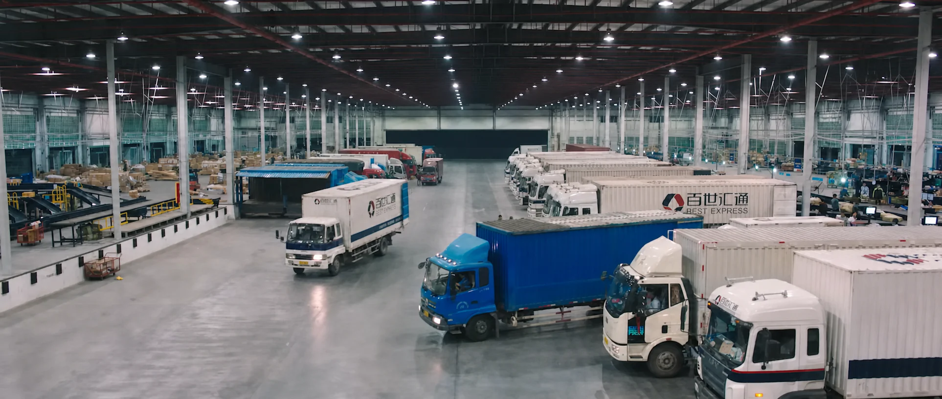 Trucks and delivery vehicles inside a large logistics hub.