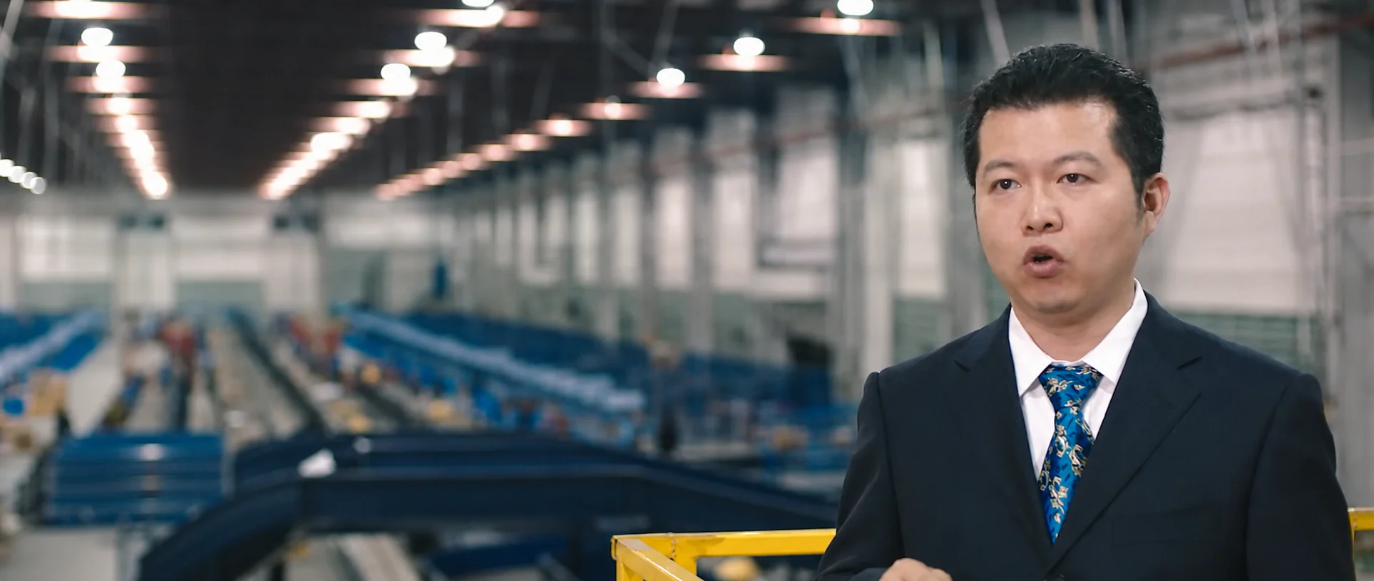 A logistics executive interviewed in front of conveyor lines.