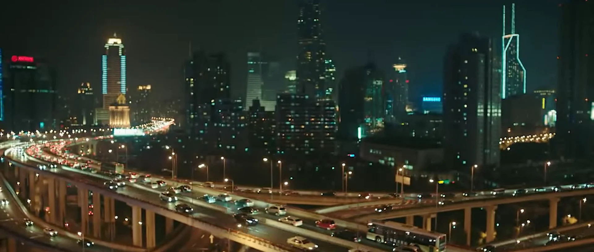 Night traffic moving through elevated roads beneath a city skyline.