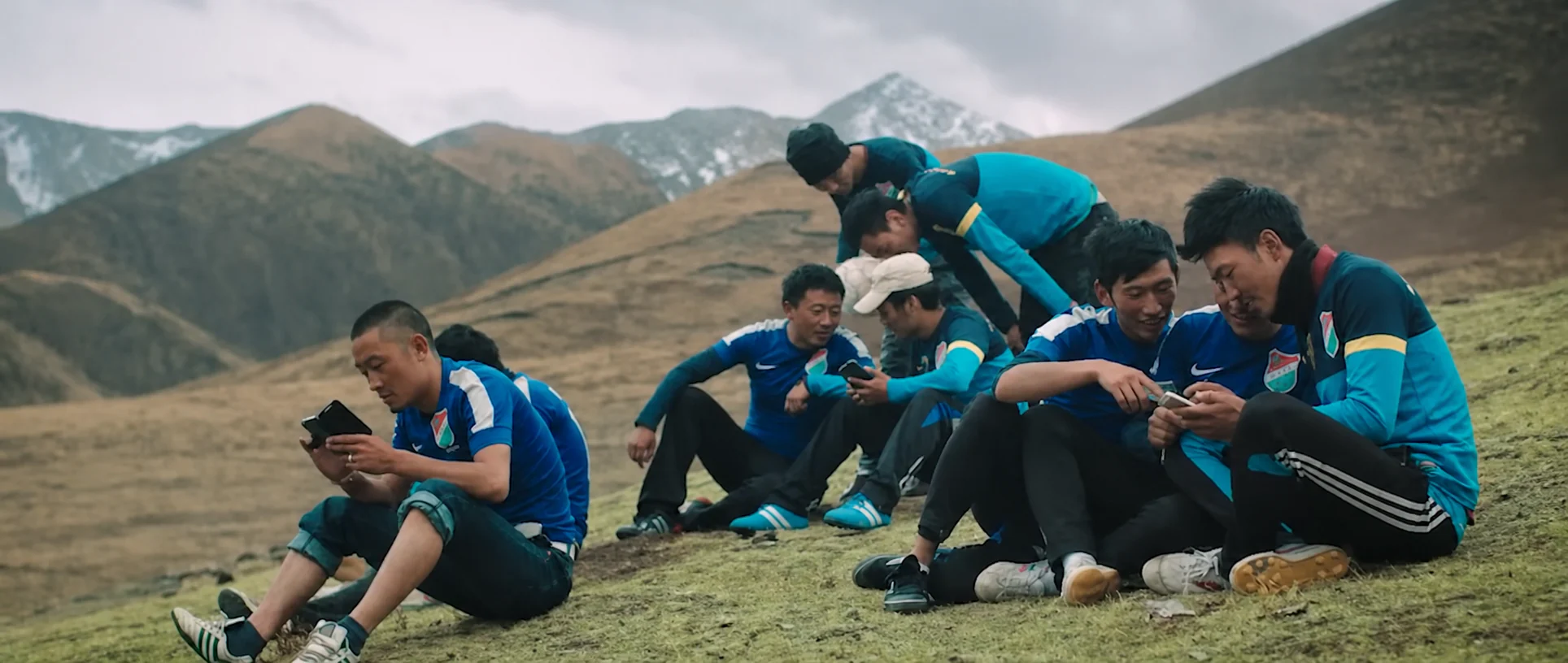 Football players gathered on grass beneath mountain ridges near Yushu.