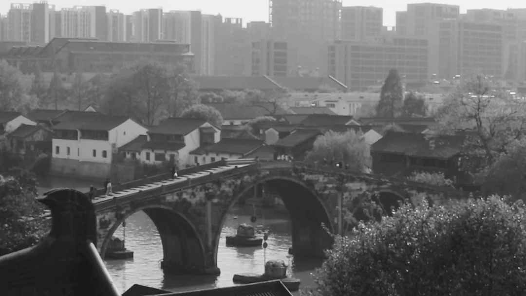 Arched bridge, waterway, traditional rooftops and distant city buildings in the Hangzhou project footage.