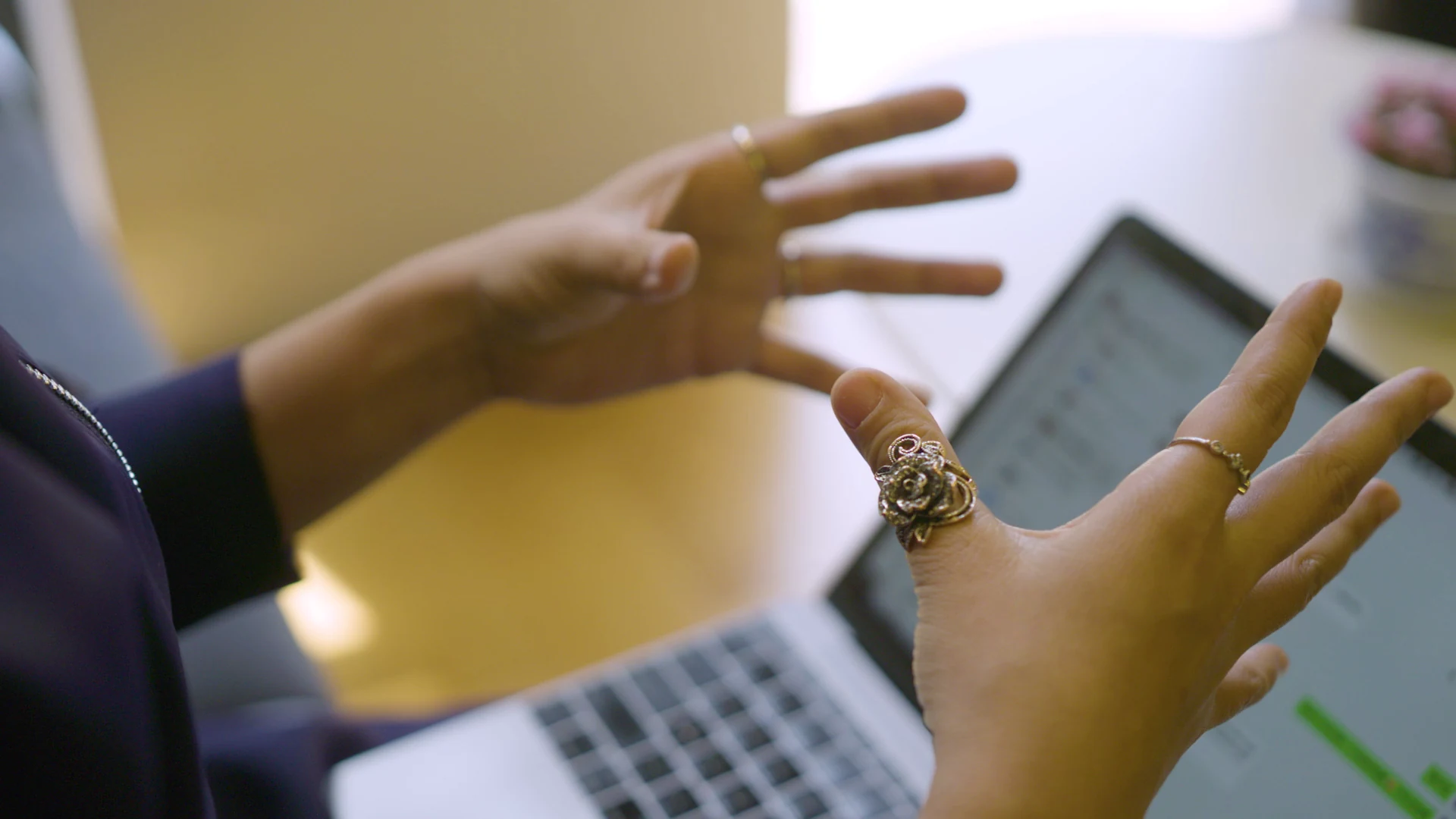 Hands gesturing beside an open laptop during a workplace conversation.