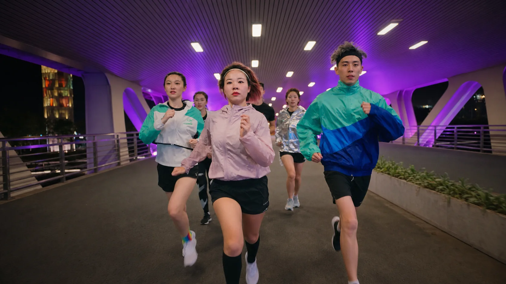 One Crew running as a group toward the camera beneath purple bridge lights
