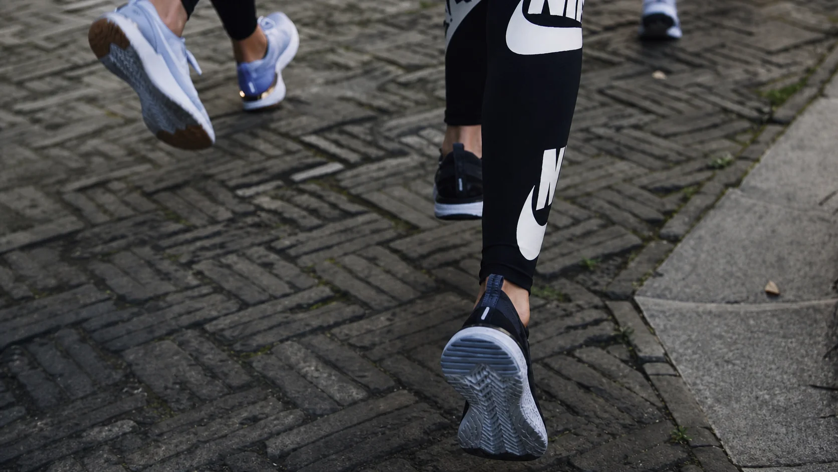 Close view of One Crew runners' shoes moving over brick pavement