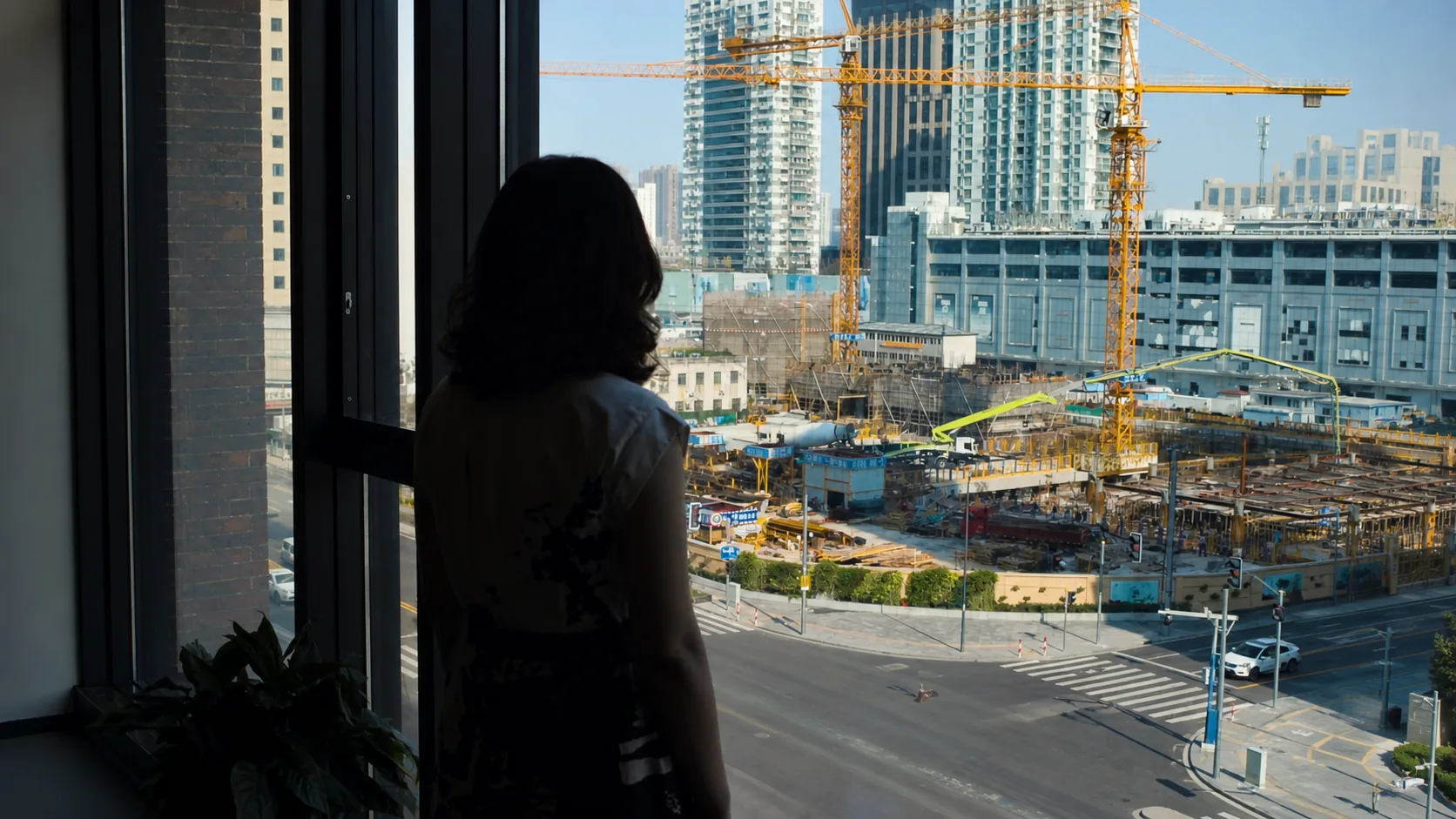 Silhouetted person at a window overlooking cranes and high-rise construction in Shanghai