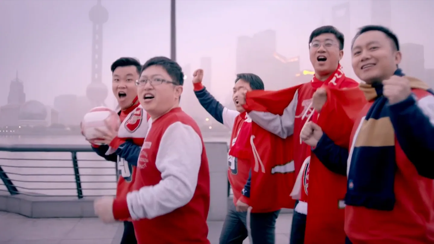 Five Shanghai Arsenal supporters moving together on the Bund with the skyline behind them
