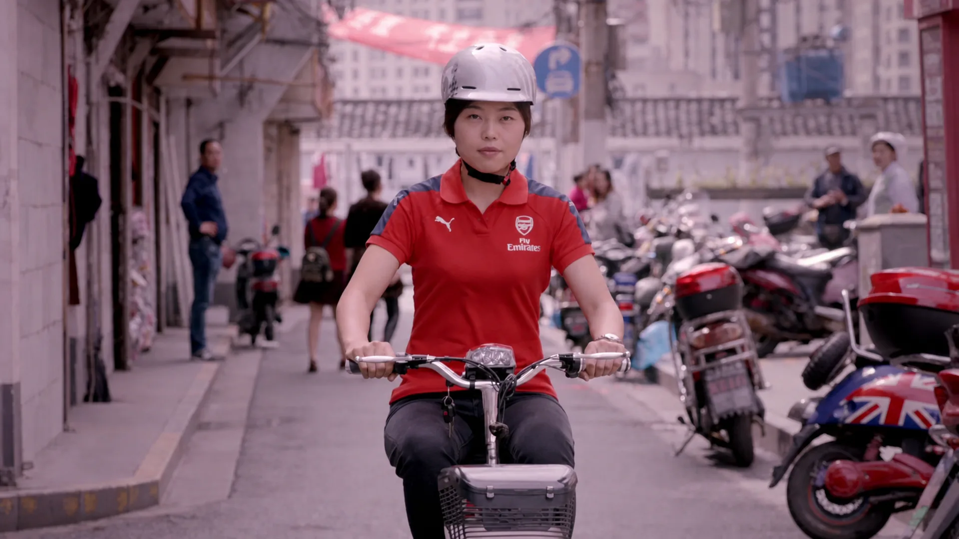 Shanghai Arsenal supporter riding an e-bike toward camera through a neighborhood street
