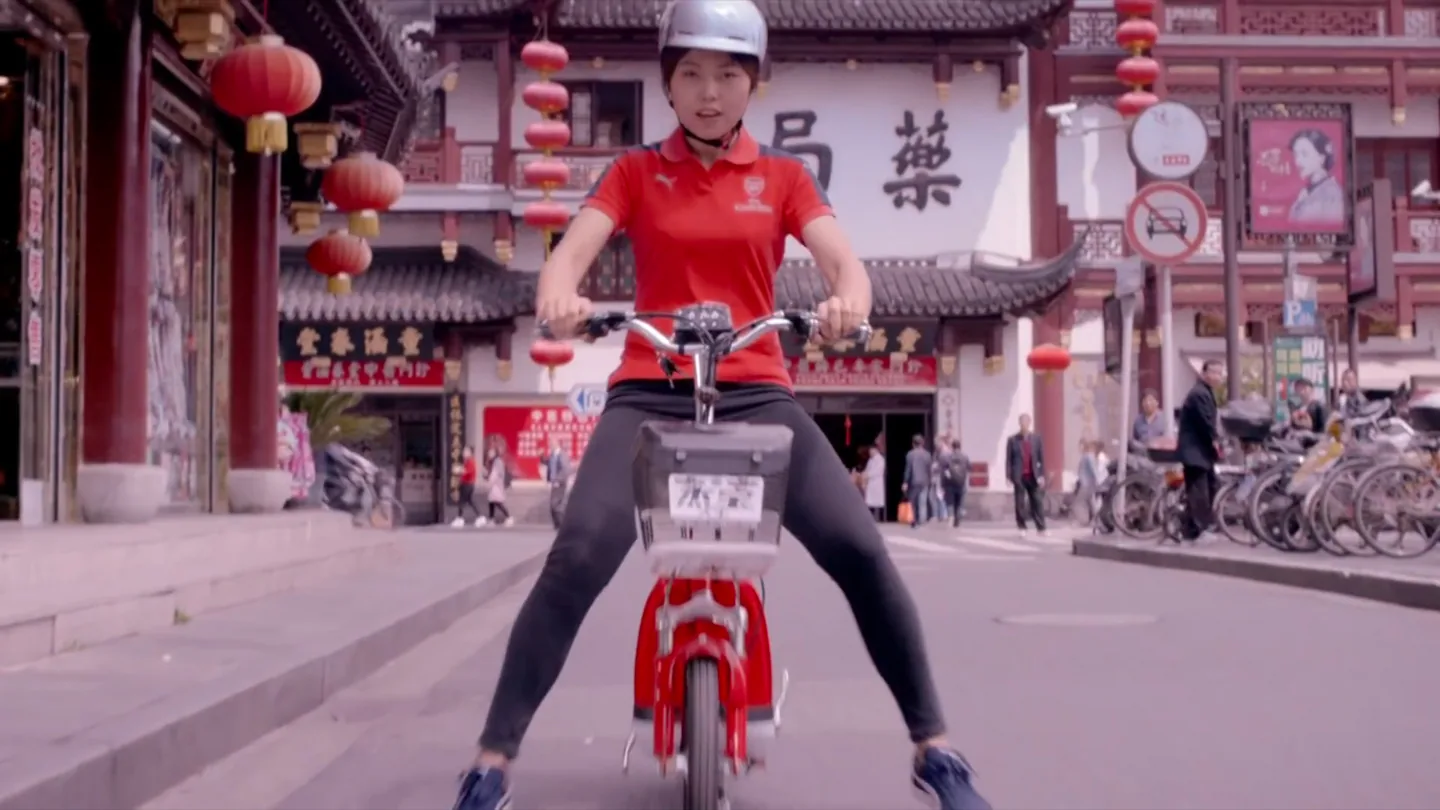 Shanghai Arsenal supporter riding a red e-bike through a traditional commercial street