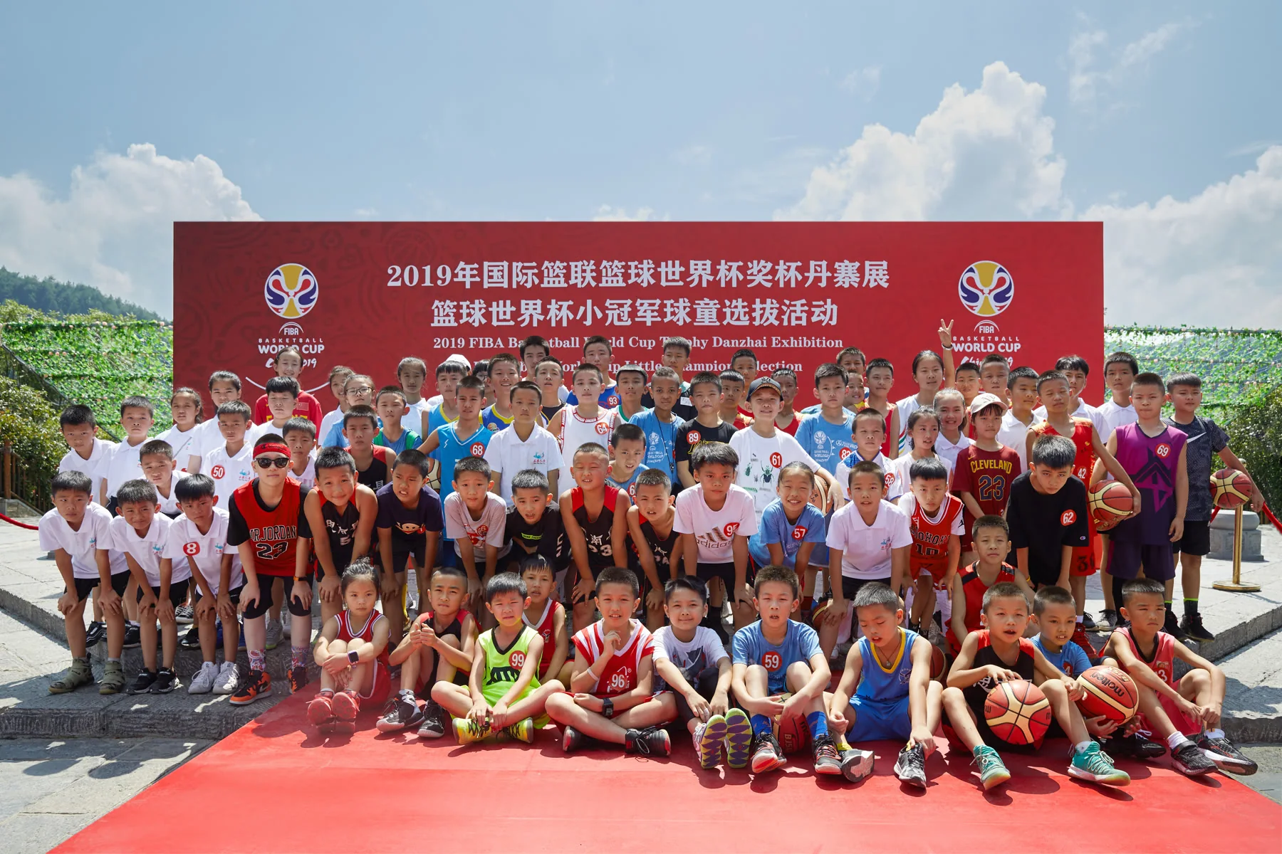 Little Champions participants pose beneath a 2019 FIBA Basketball World Cup event banner