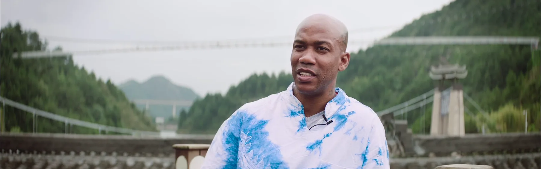 An adult participant speaks outdoors with the Danzhai landscape behind him