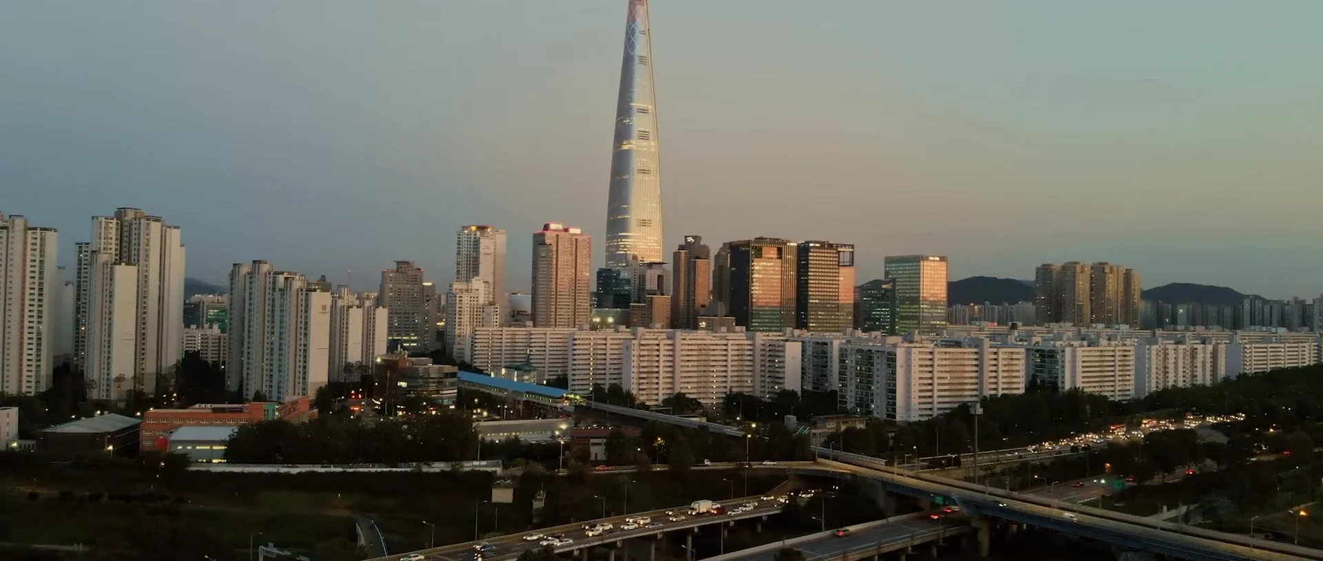 A tall tapered tower rises above a city skyline at dusk.