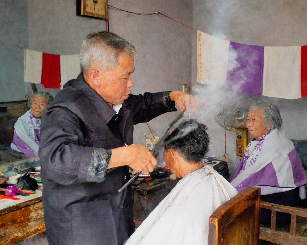 Barber cutting a client's hair inside a modest interior in China