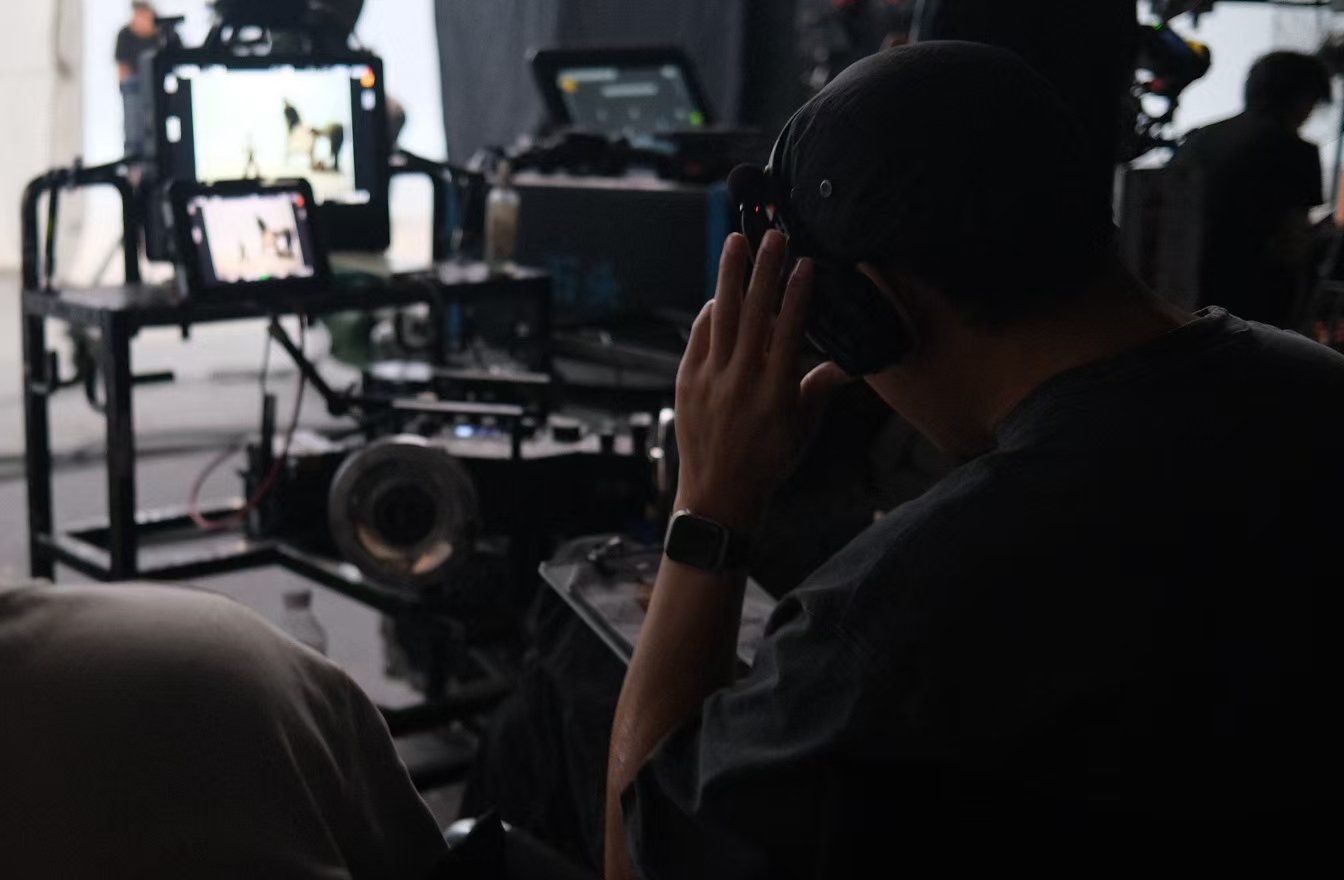 A person wearing headphones sits beside monitors, equipment cases and cables in a studio.