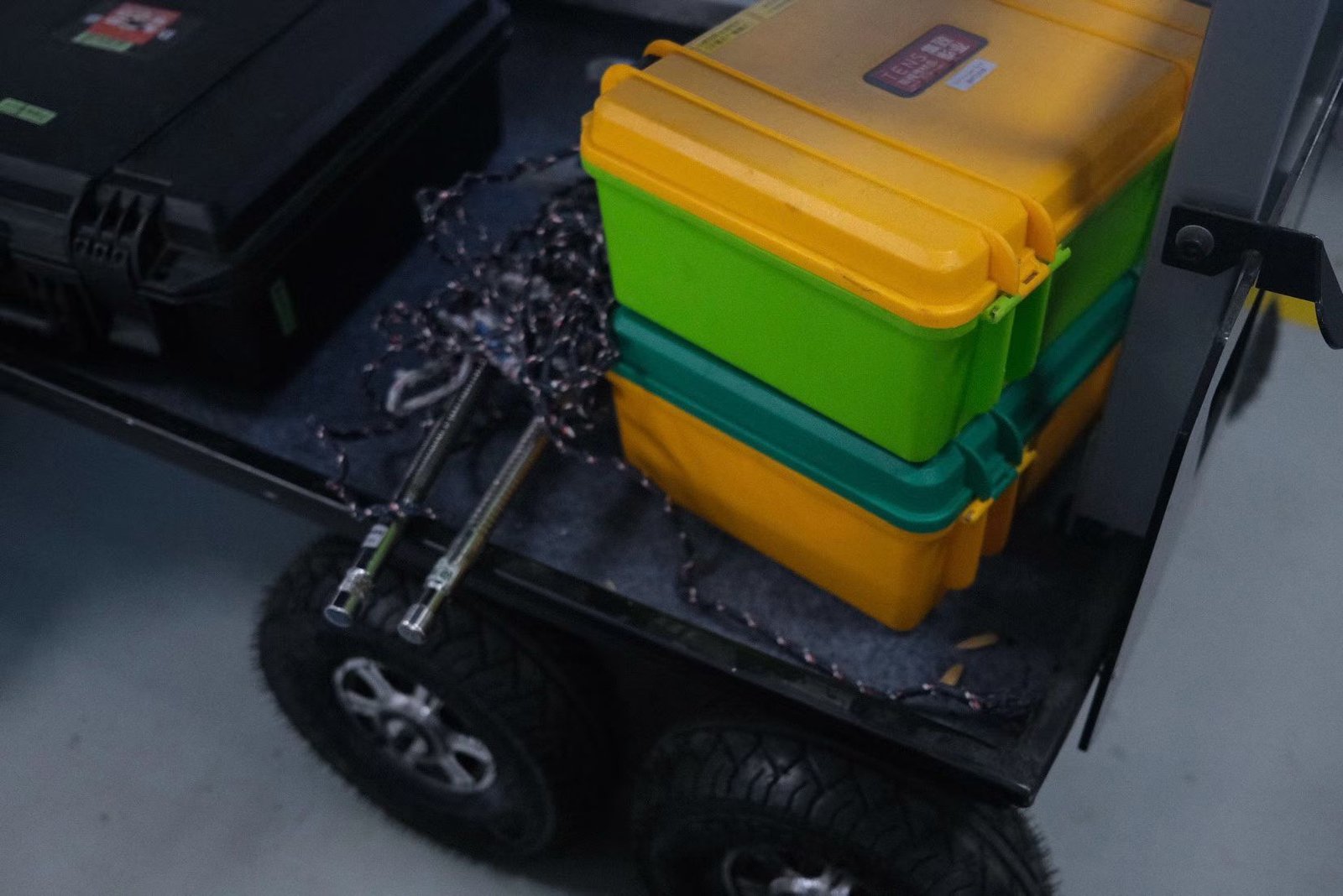 Black equipment cases and bright storage boxes stacked on a wheeled trolley.
