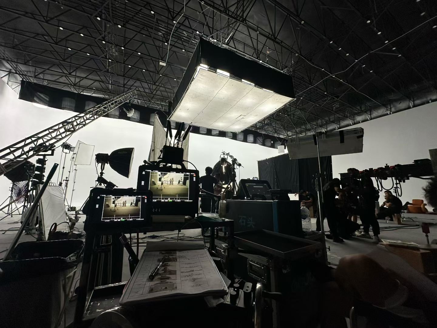 A wide studio view with overhead lighting, camera equipment, monitors and people around the set.