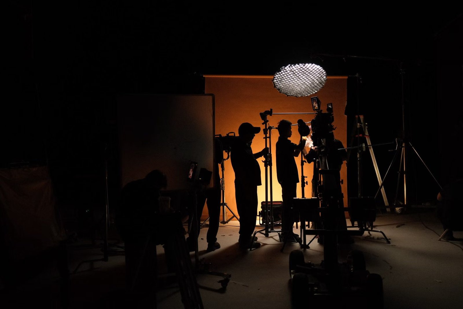 People work around a camera and lighting equipment in silhouette against an orange studio backdrop.