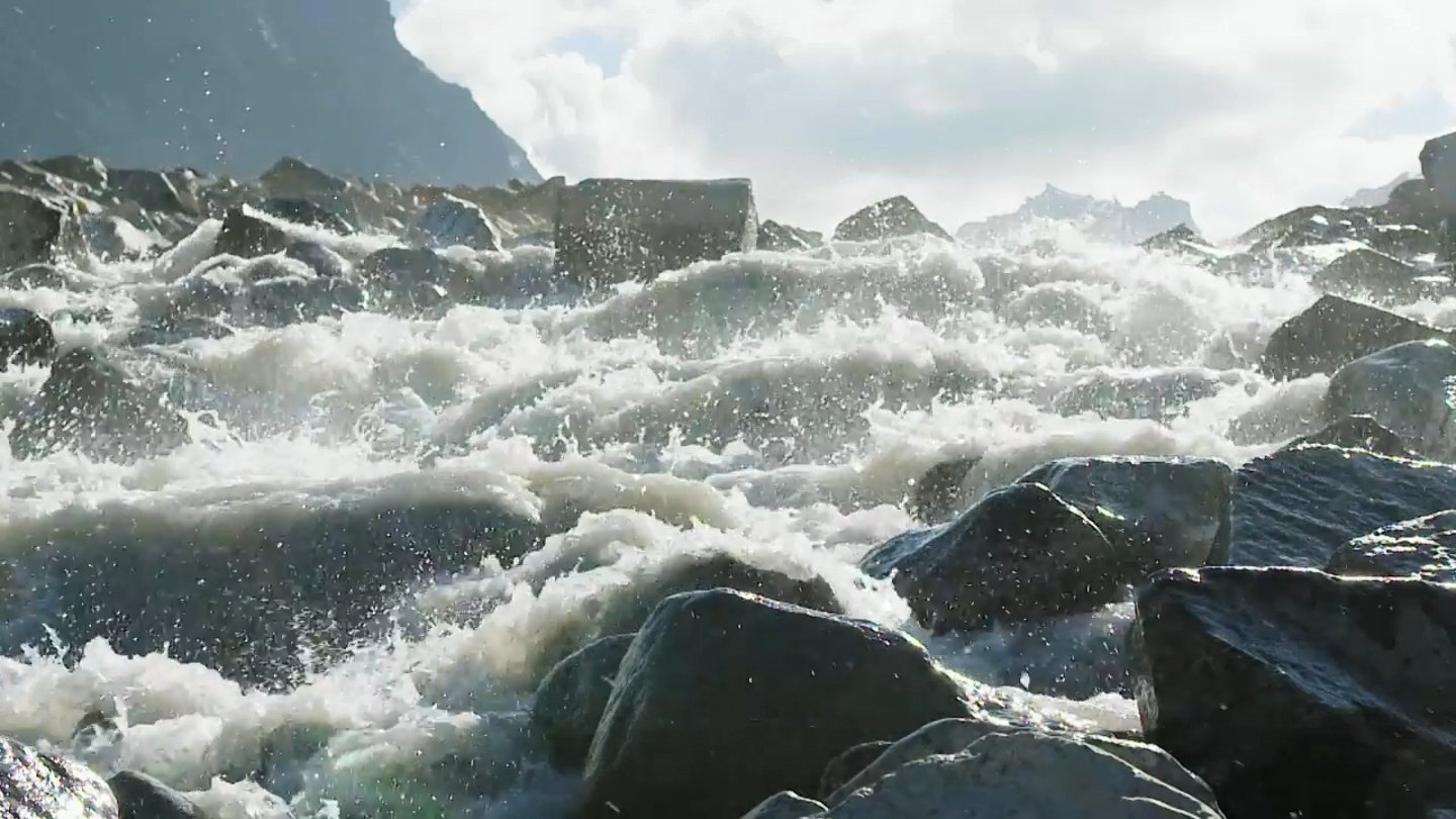Fast water breaking over dark rocks. Programme still.
