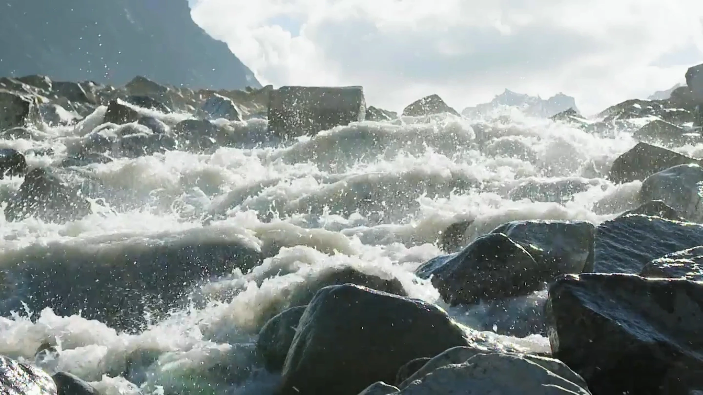 Fast water breaking over dark rocks. Programme still.