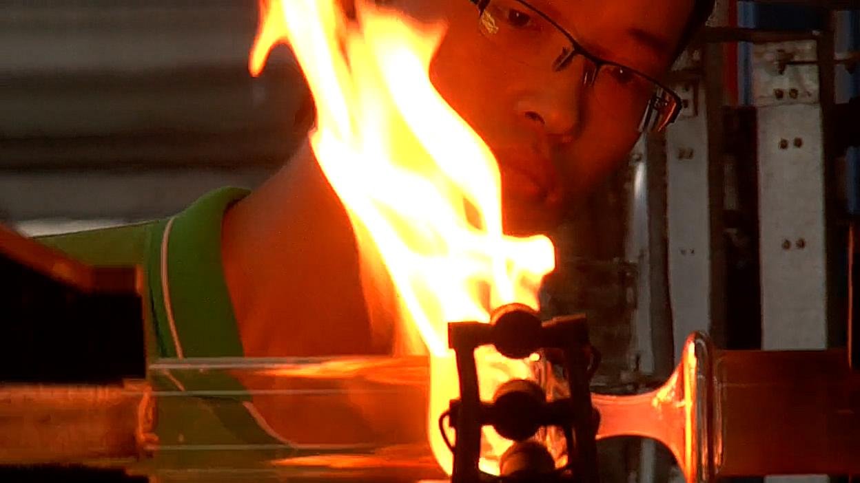 A worker heating glass tubing in a flame. Film still.