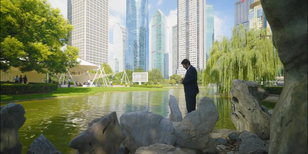Man in a business suit standing by a serene lake in a modern city park with skyscrapers in the background.