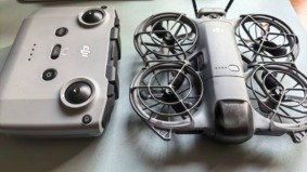 Consumer drone with propeller guards placed next to its remote controller on an indoor surface.