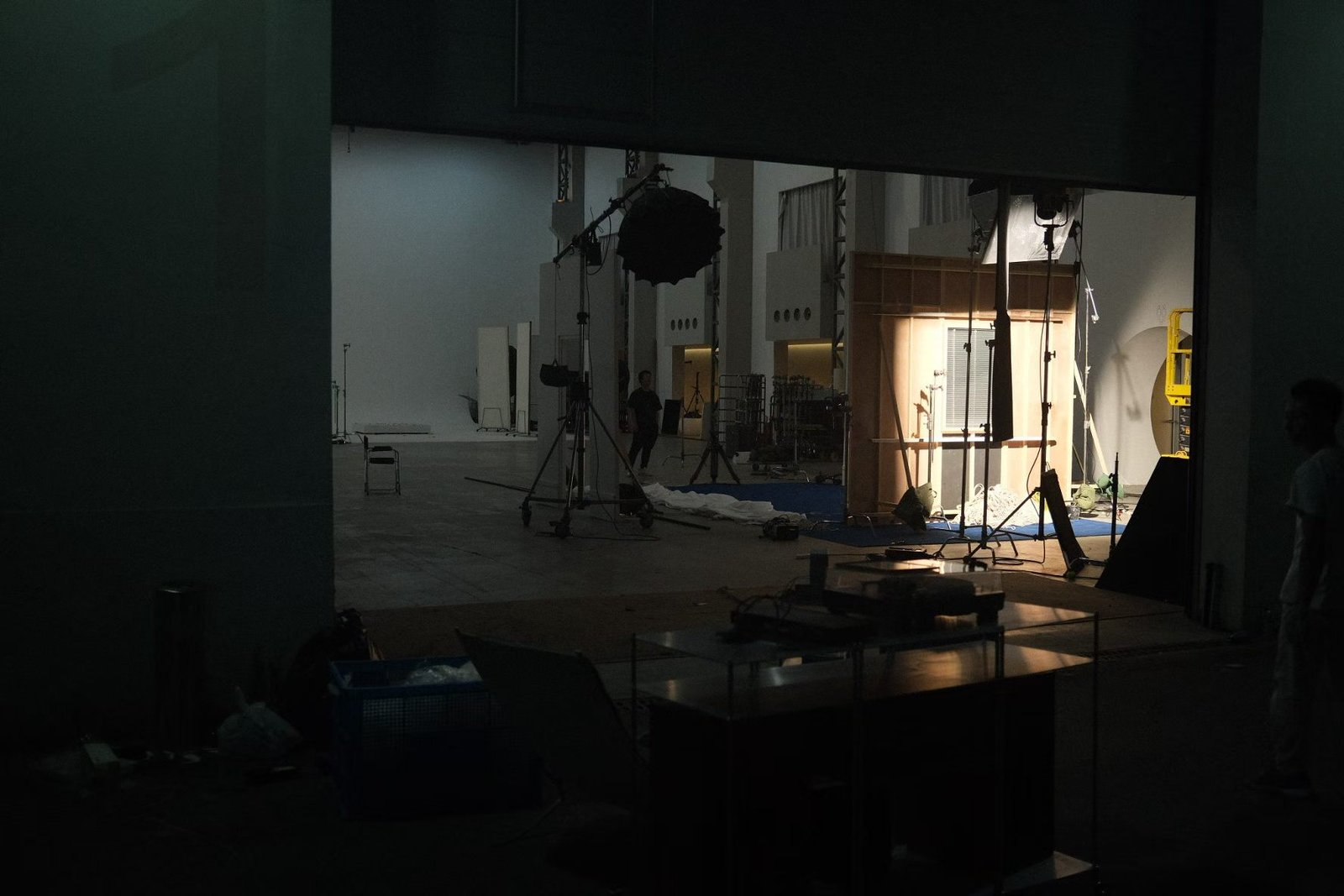 A partially open shutter reveals a studio set with a window wall and lighting stands.