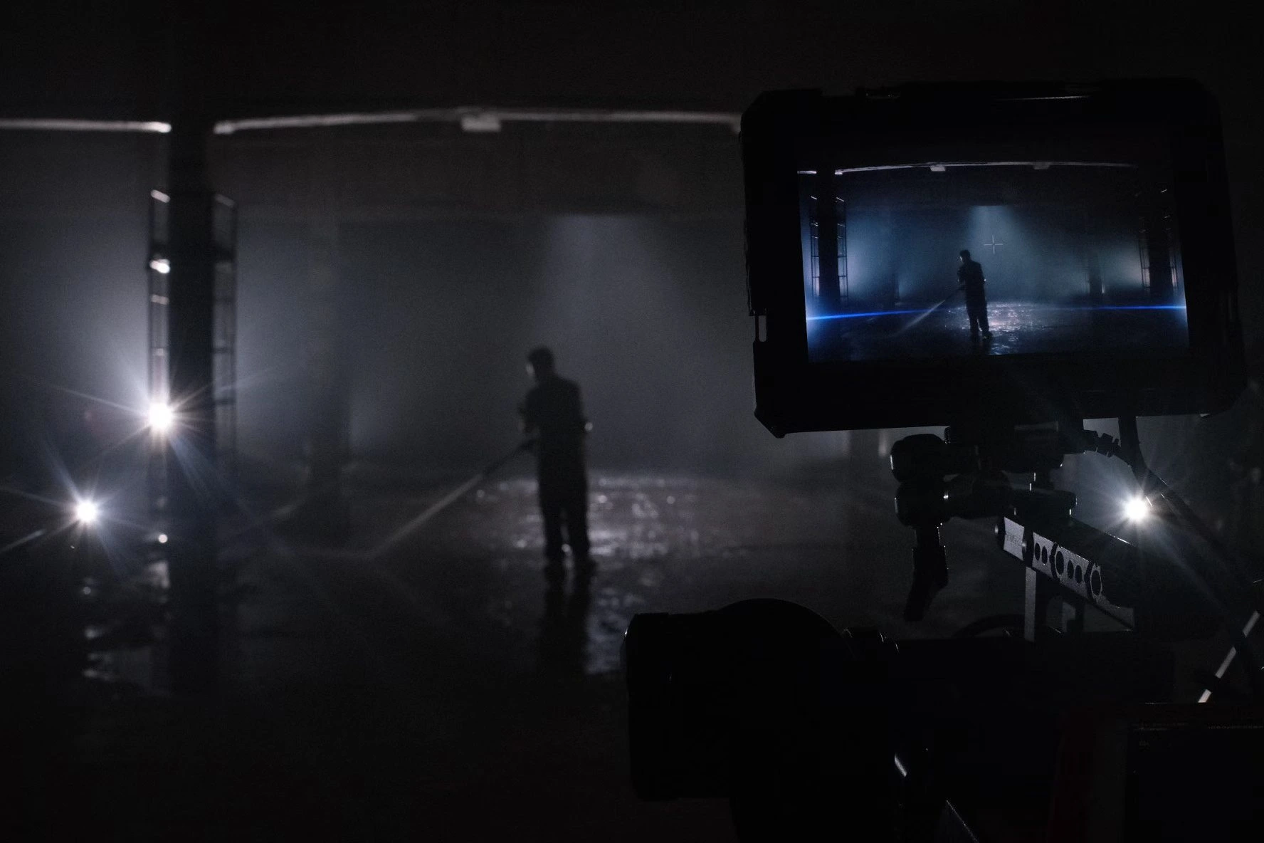 A camera monitor frames a silhouetted figure on a hazy, backlit studio set.